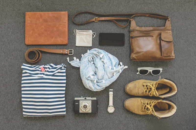 Kleidungsstücke, Schuhe, Gürtel, Tasche, Uhr, Sonnenbrille auf grauem Teppich